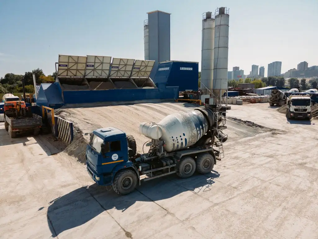 A truck mixer standing at a batching plant with aggregate stockpiles behind